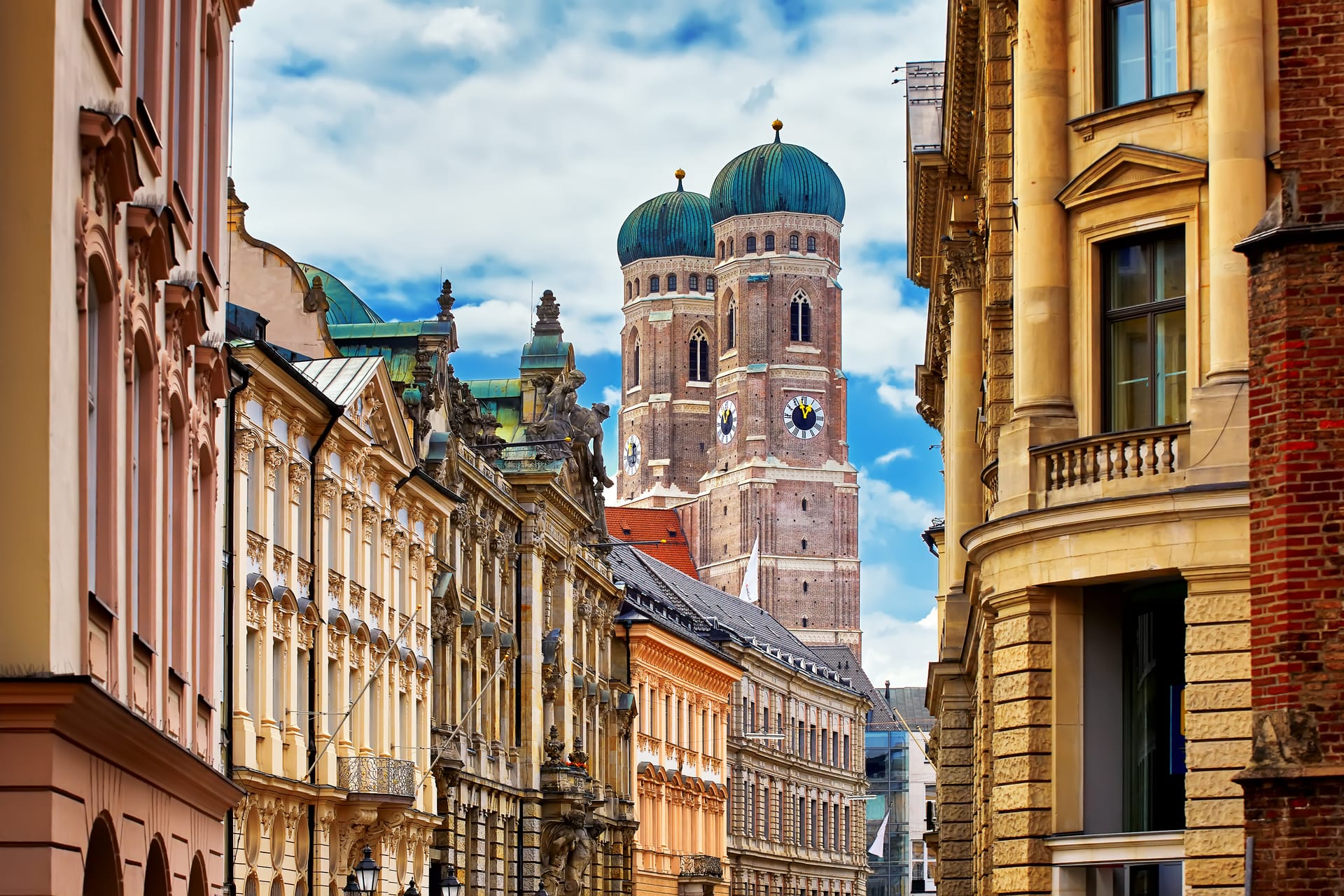 Historic Munich street view with the iconic twin turquoise domes of Frauenkirche cathedral rising above colourful buildings.