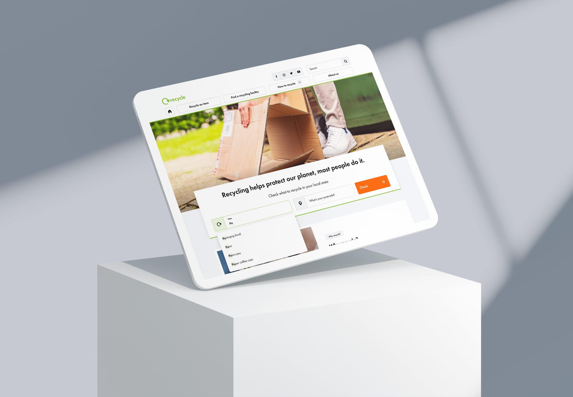 Tablet displaying Recycle website with cardboard box image and "Recycling helps protect our planet" message on white pedestal.