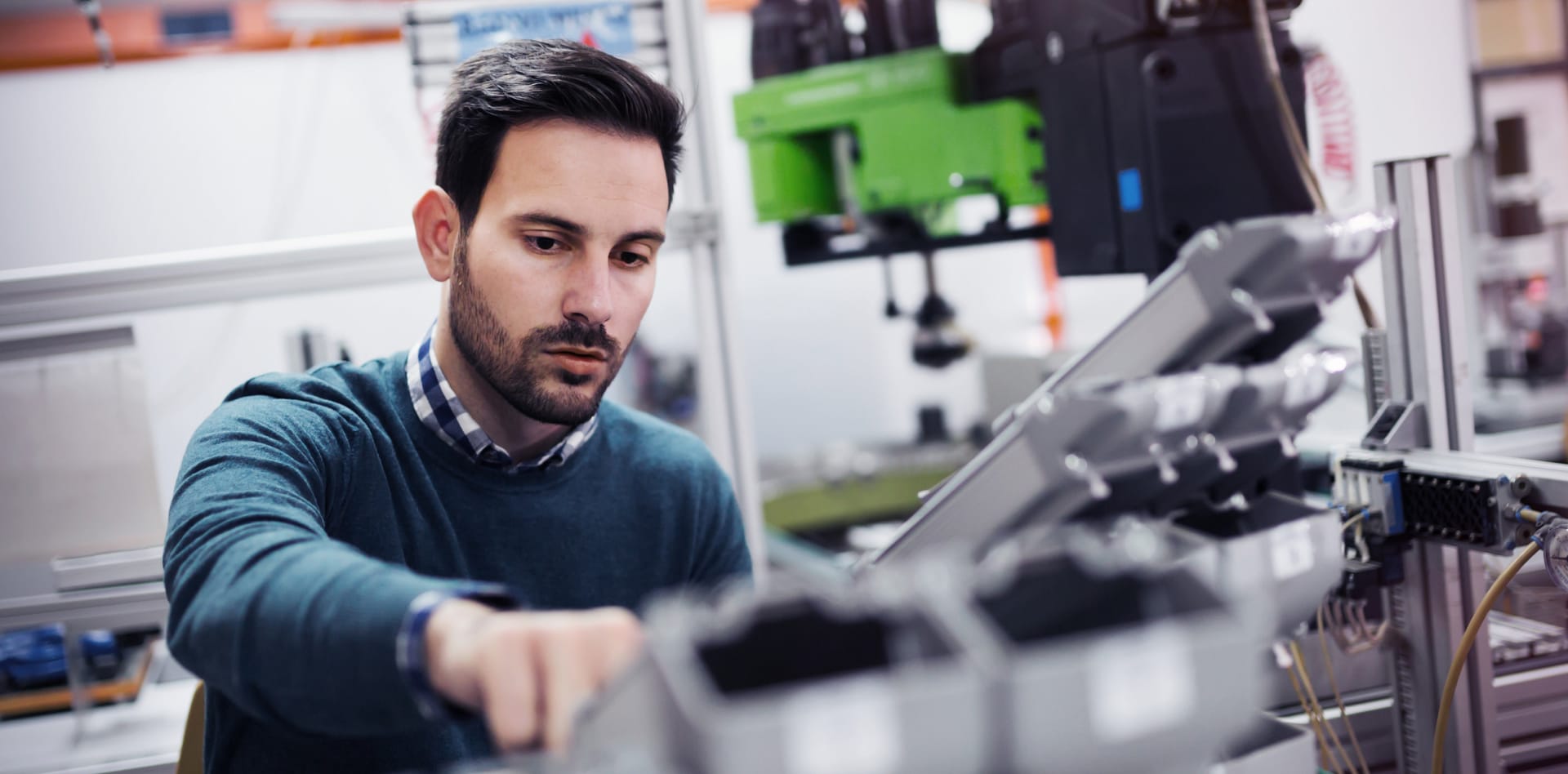 Person in blue jumper operating technical equipment in a manufacturing facility with green machinery in background.