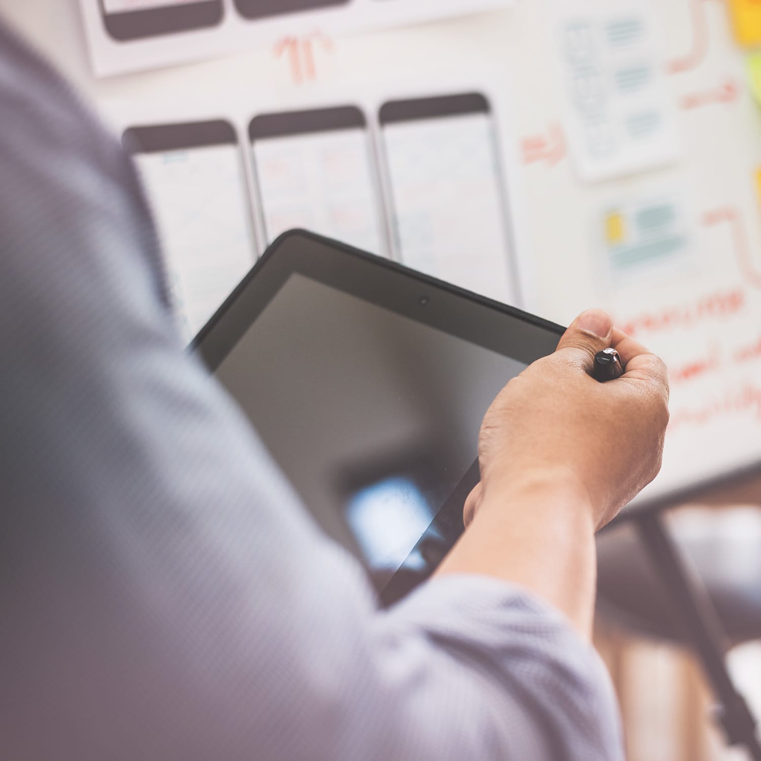 Person holding tablet device while reviewing project planning boards with colourful charts in background.