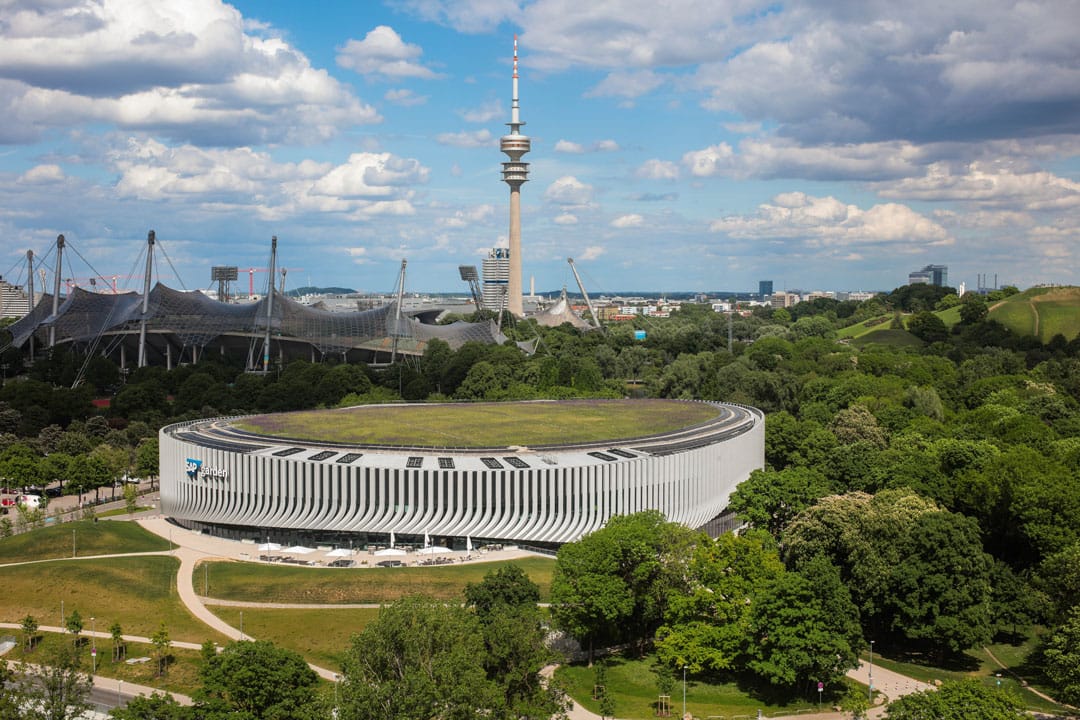 Aerial view of Munich with Olympic Park, featuring a modern circular building with green roof and the Olympic Tower.