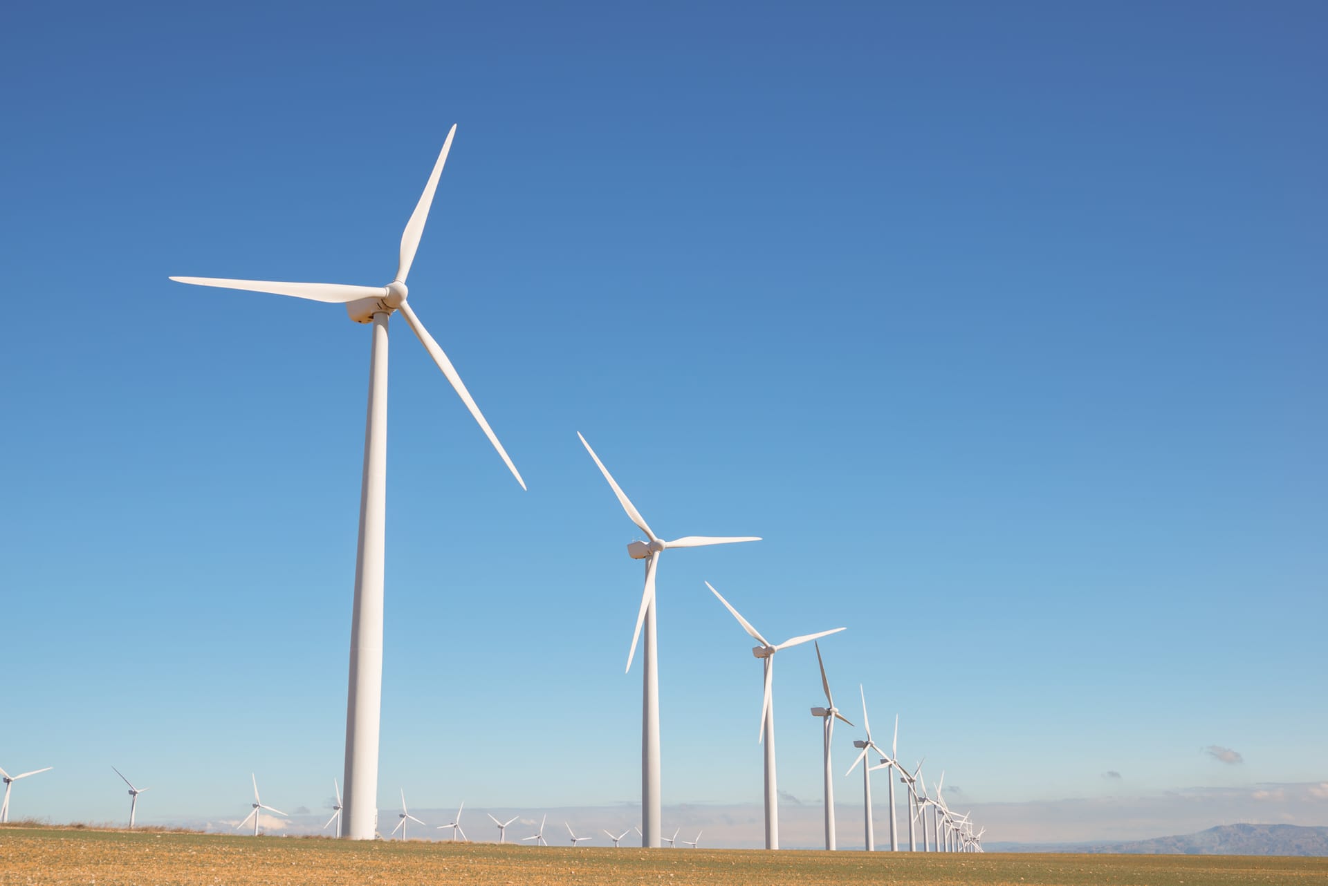 White wind turbines in a row across a flat landscape against a clear blue sky, generating renewable energy.